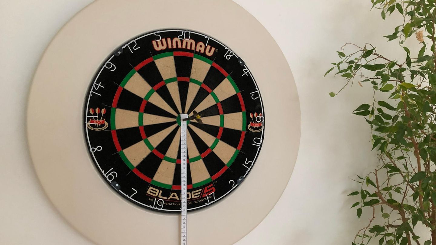 Dartscheibe aufhängen: Dartscheibe mit weißem Surround und Maßband hängt an der Wand