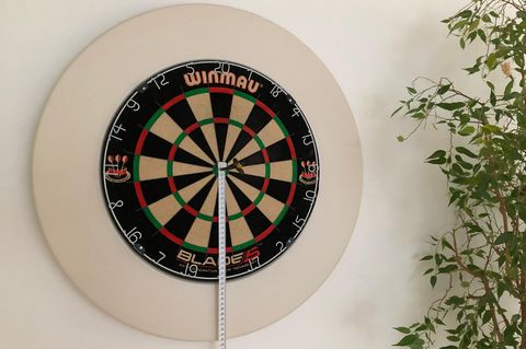 Dartscheibe aufhängen: Dartscheibe mit weißem Surround und Maßband hängt an der Wand