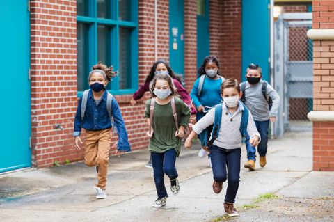 Grundschüler mit Masken rennen aus einer Schule