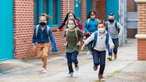 Grundschüler mit Masken rennen aus einer Schule