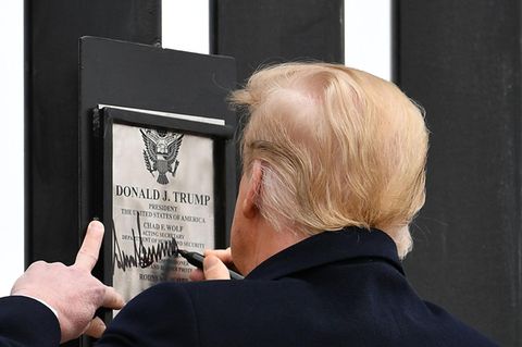 US-Präsident Donald Trump ist von hinten zu sehen, während er auf einer Urkunde mit seinem Namen an einer Mauer unterschreibt