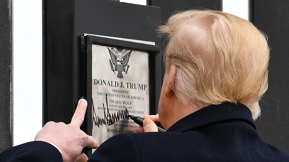 US-Präsident Donald Trump ist von hinten zu sehen, während er auf einer Urkunde mit seinem Namen an einer Mauer unterschreibt