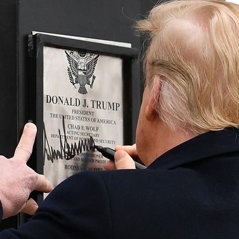US-Präsident Donald Trump ist von hinten zu sehen, während er auf einer Urkunde mit seinem Namen an einer Mauer unterschreibt