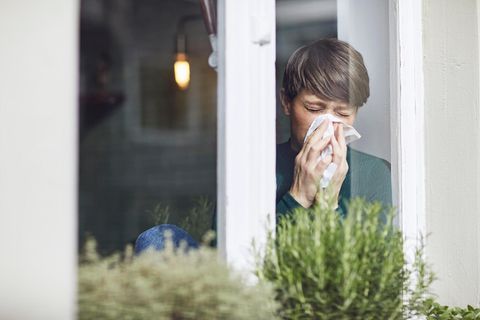 Frau putzt sich die Nase am Fenster